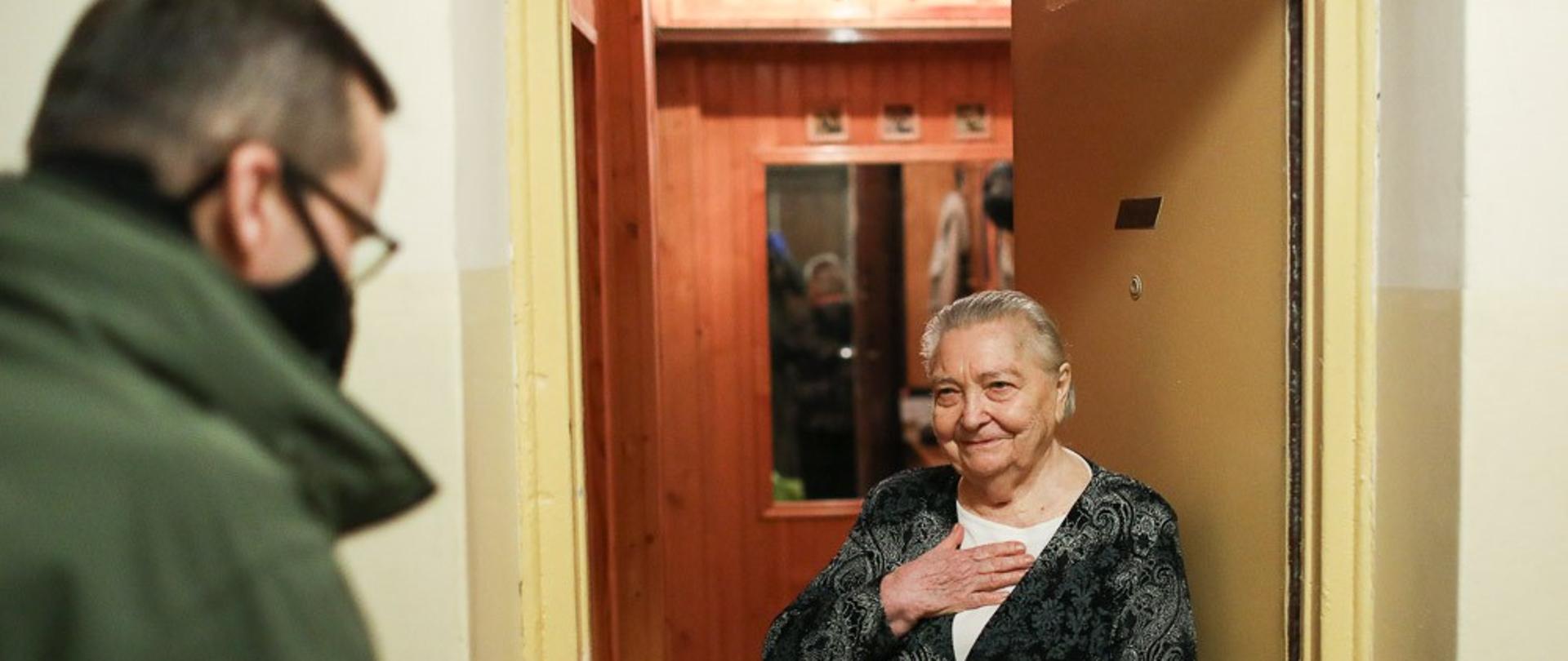 Seniorka w drzwiach do mieszkania rozmawia z premierem.