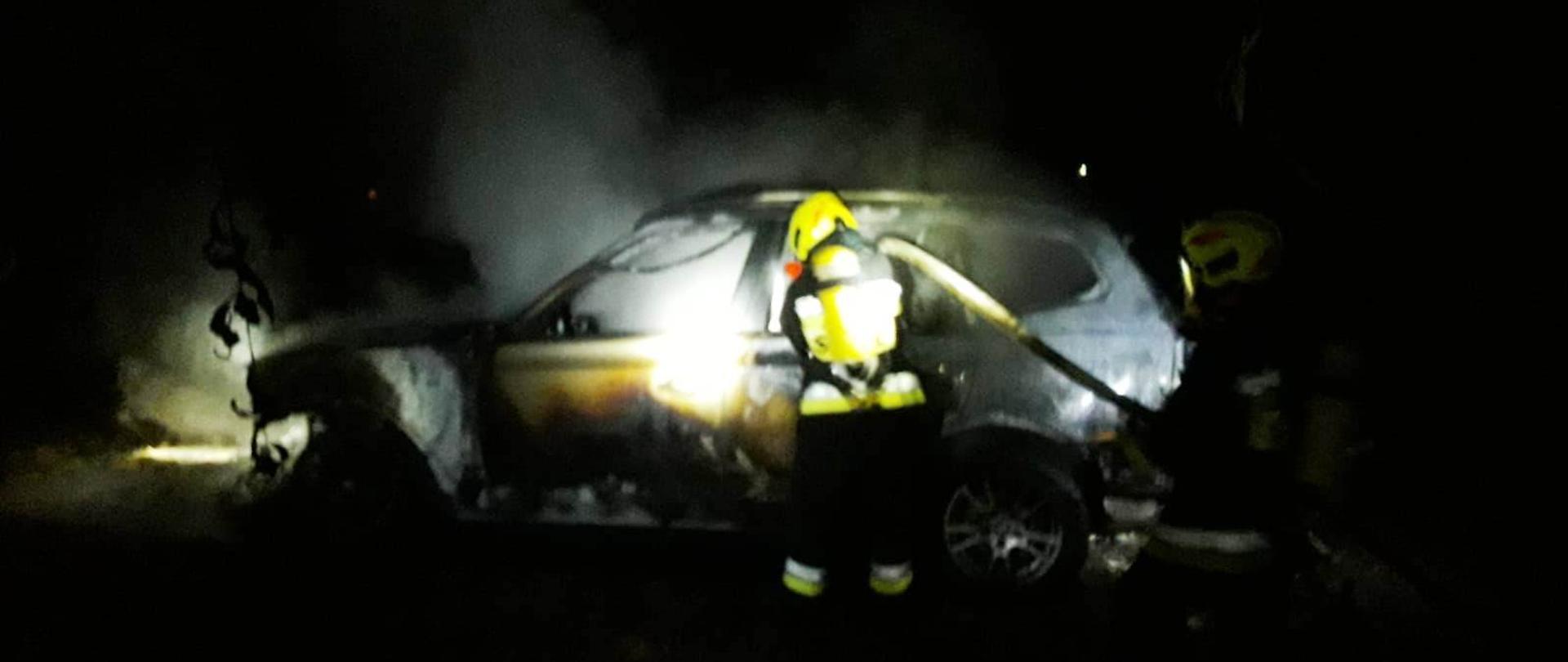 Strażacy gaszą pożar samochodu.