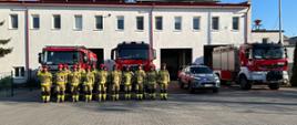 Na zdjęciu widać strażaków którzy oddali hołd poległym strażakom z Ukrainy. Strażacy stoją przed remizą i przed samochodami. 