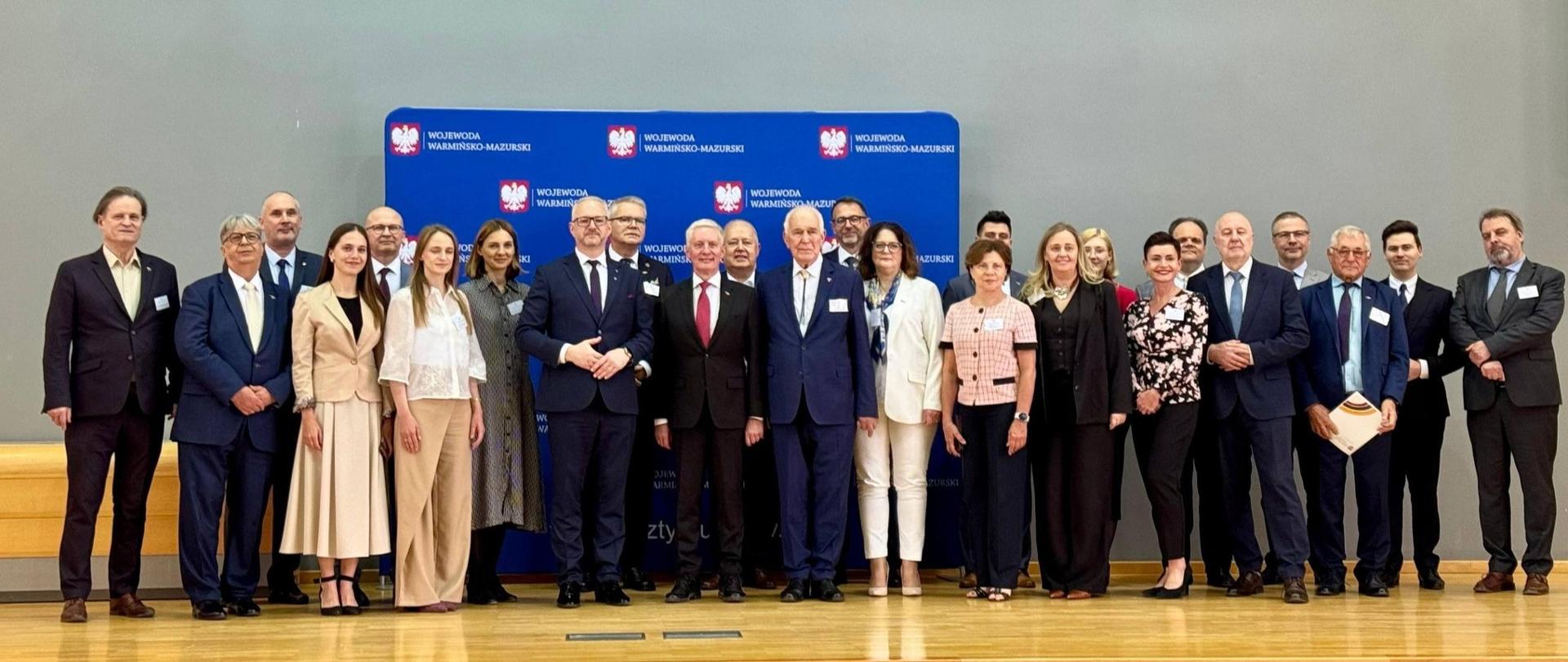 grupa oficjeli stoi na scenie, pozują do zdjęcia 