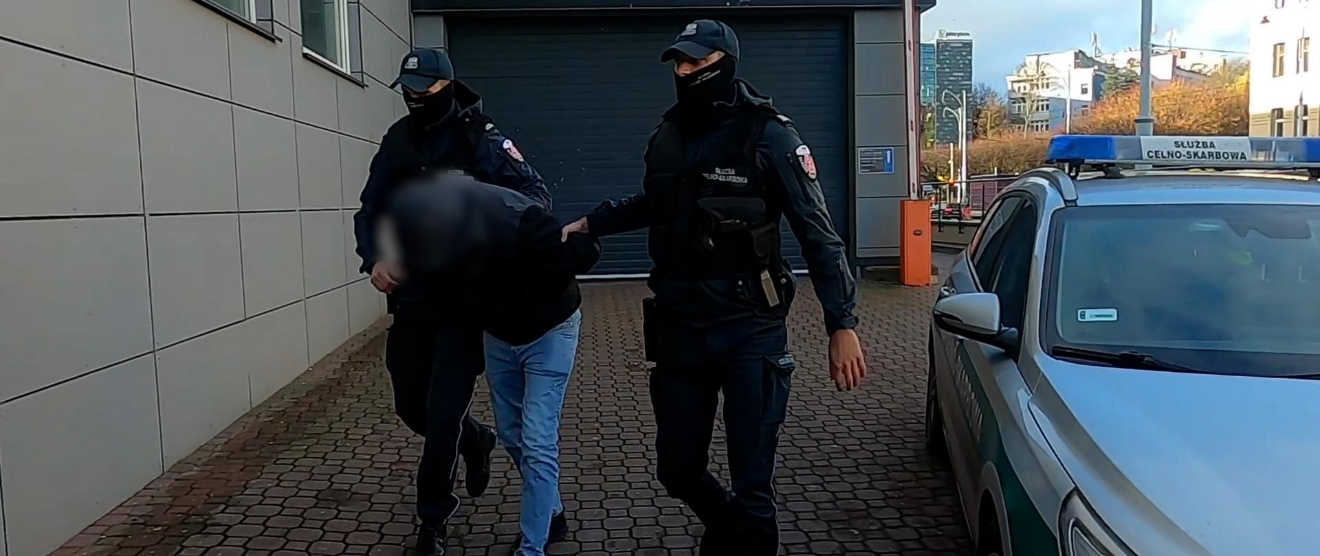 dwóch funkcjonariuszy doprowadza podejrzanego do aresztu.