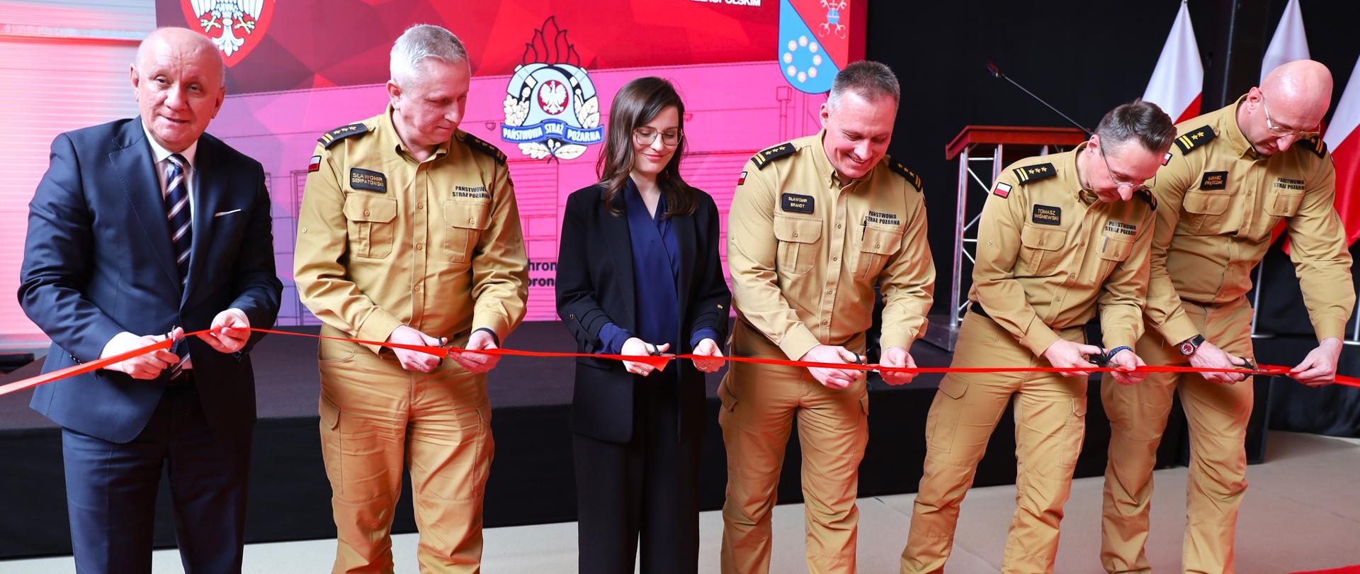 Czterech strażaków, jeden mężczyzna i kobieta w cywilu przecinają wstęgę. 