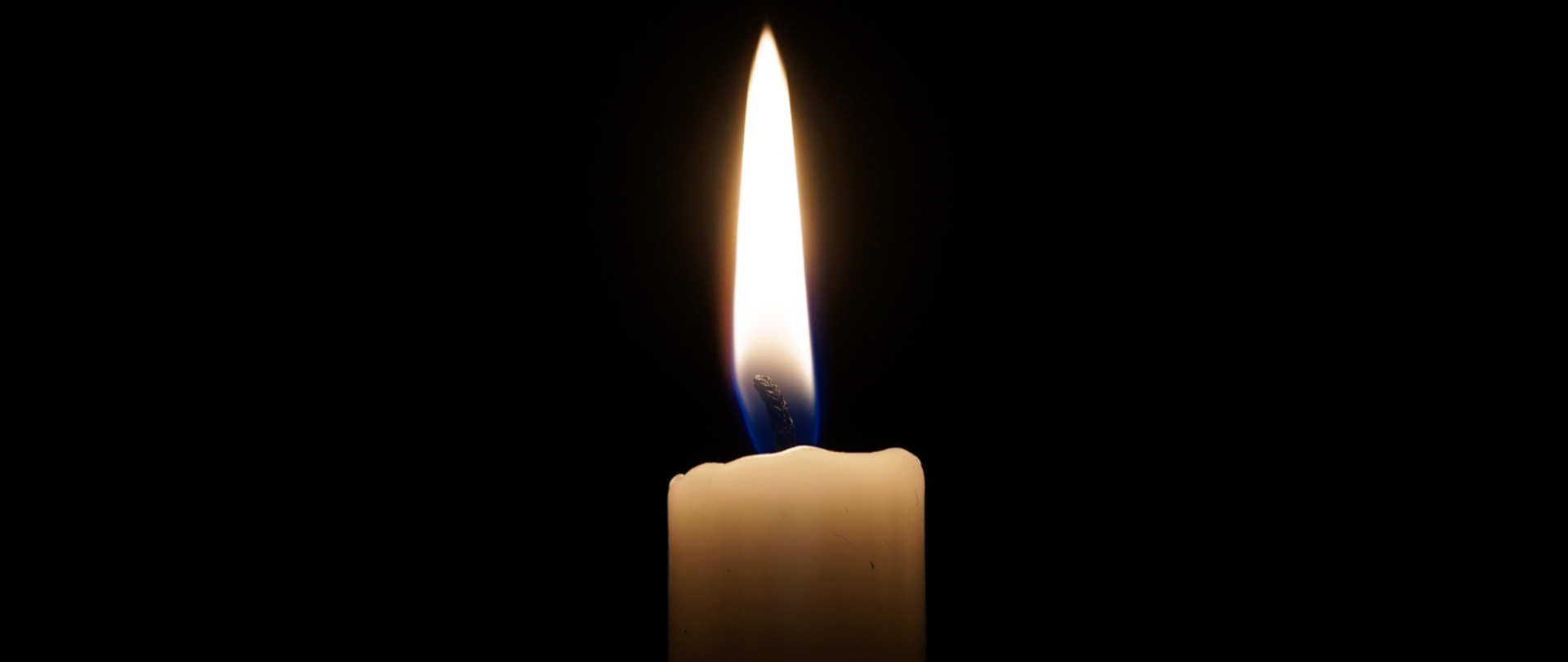 Zdjęcie przedstawia palącą się świecę na czarnym tle - symbolizującą żałobę