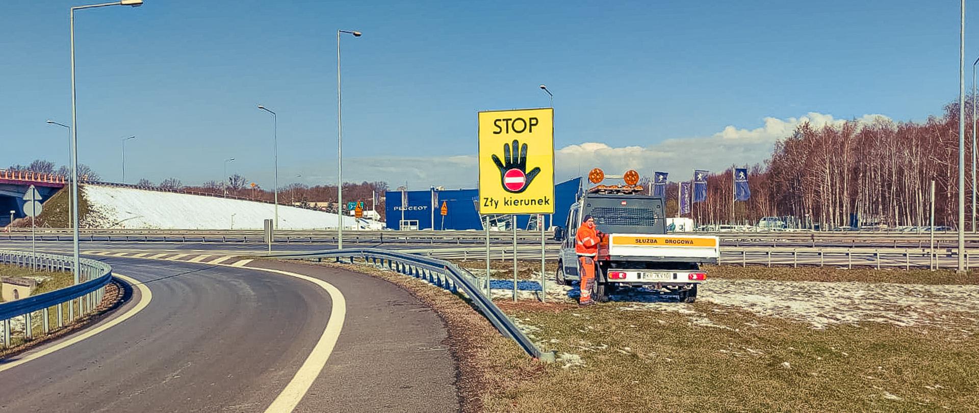 Fotografia z poziomu teremu ustawionego znaku Stop Zły Kierunek na łącznicy węzła Wapienica w ciągu drogi ekspresowa S52. Charakterystyczną dużą żółtą tablicę z napisem STOP Zły kierunek i symbolem dłoni z umieszczonym na niej piktogramem znaku zakaz wjazdu zlokalizowano w centralnej części fotografii . 