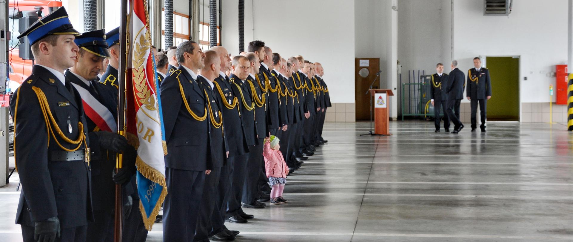 Funkcjonariusze PSP w ubraniach galowych stoją w garażu na Jednostce Ratowniczo - Gaśniczej nr 2