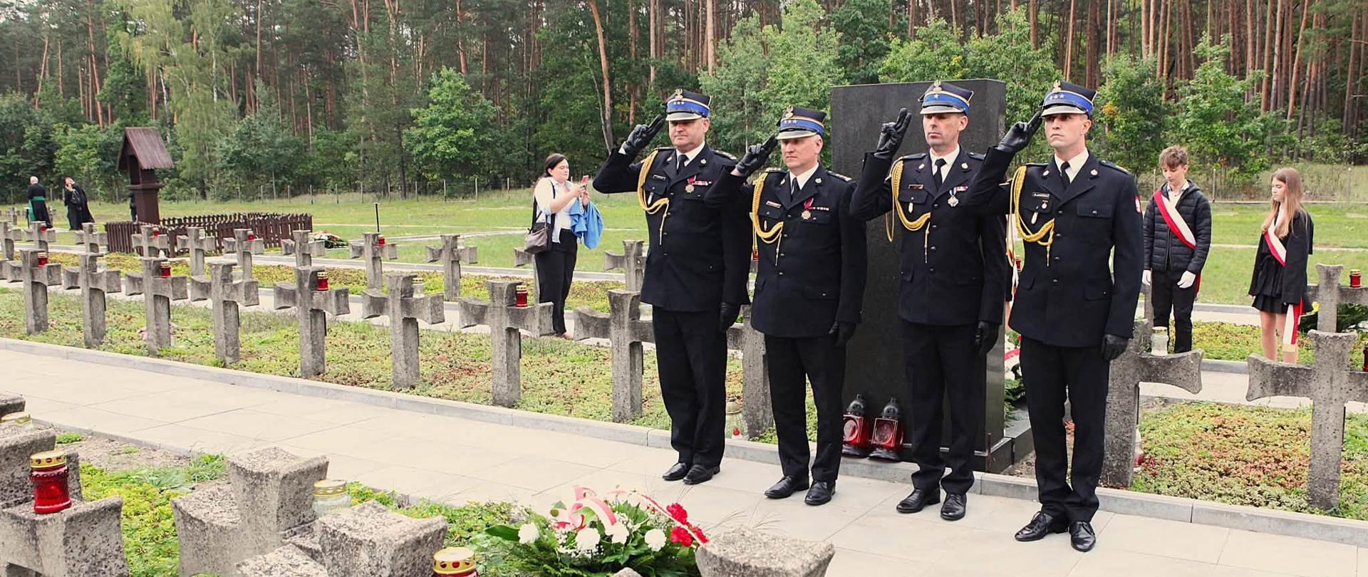 Na zdjęciu widać czterech oficerów Państwowej Straży Pożarnej w mundurach wyjściowych na Cmentarzu-Mauzoleum w Palmirach, podczas uroczystych obchodów upamiętniających zbrodnie hitlerowskie. Wśród strażaków jest Zastępca Mazowieckiego Komendanta Wojewódzkiego st. bryg. Waldemar Wysowski oraz Komendant Powiatowy PSP w Nowym Dworze Mazowieckim st. bryg. Stanisław Brzozowski 