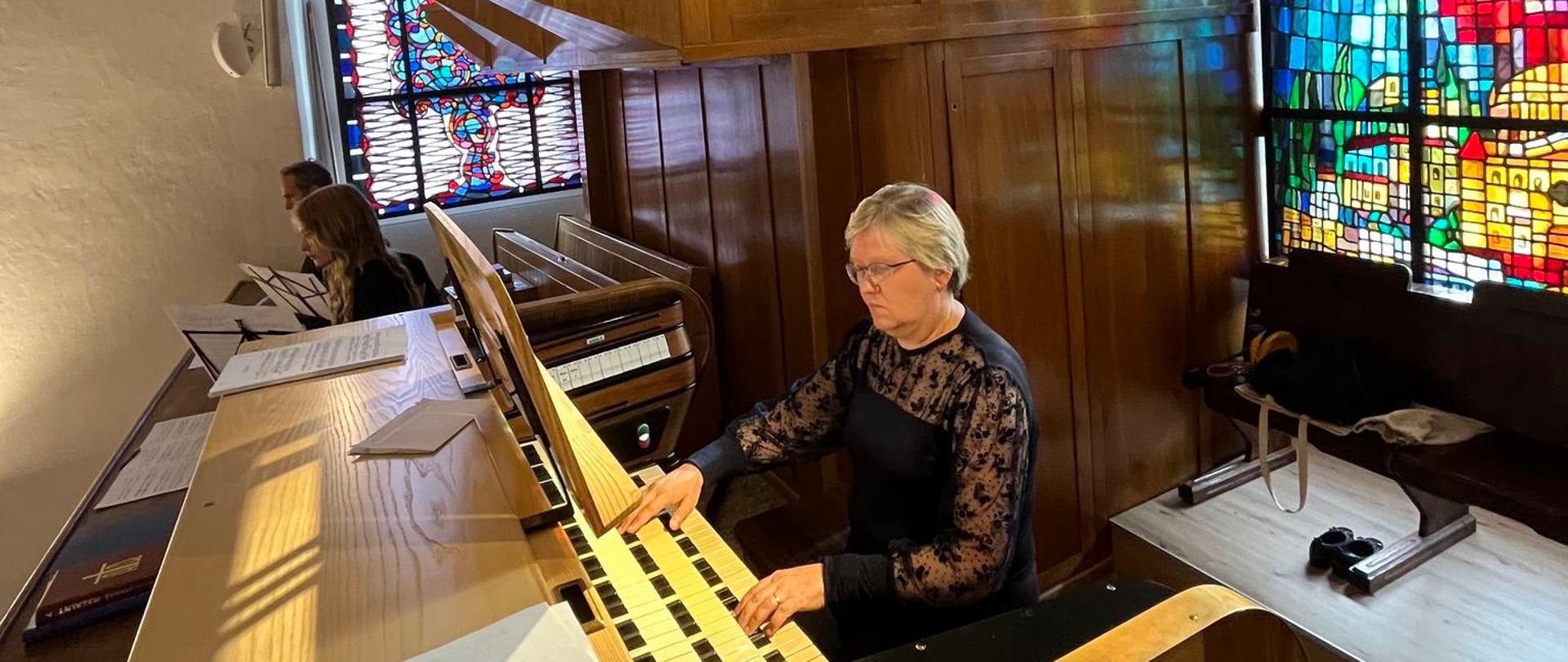 Organistka siedzi przy stole gry, w tle witraż