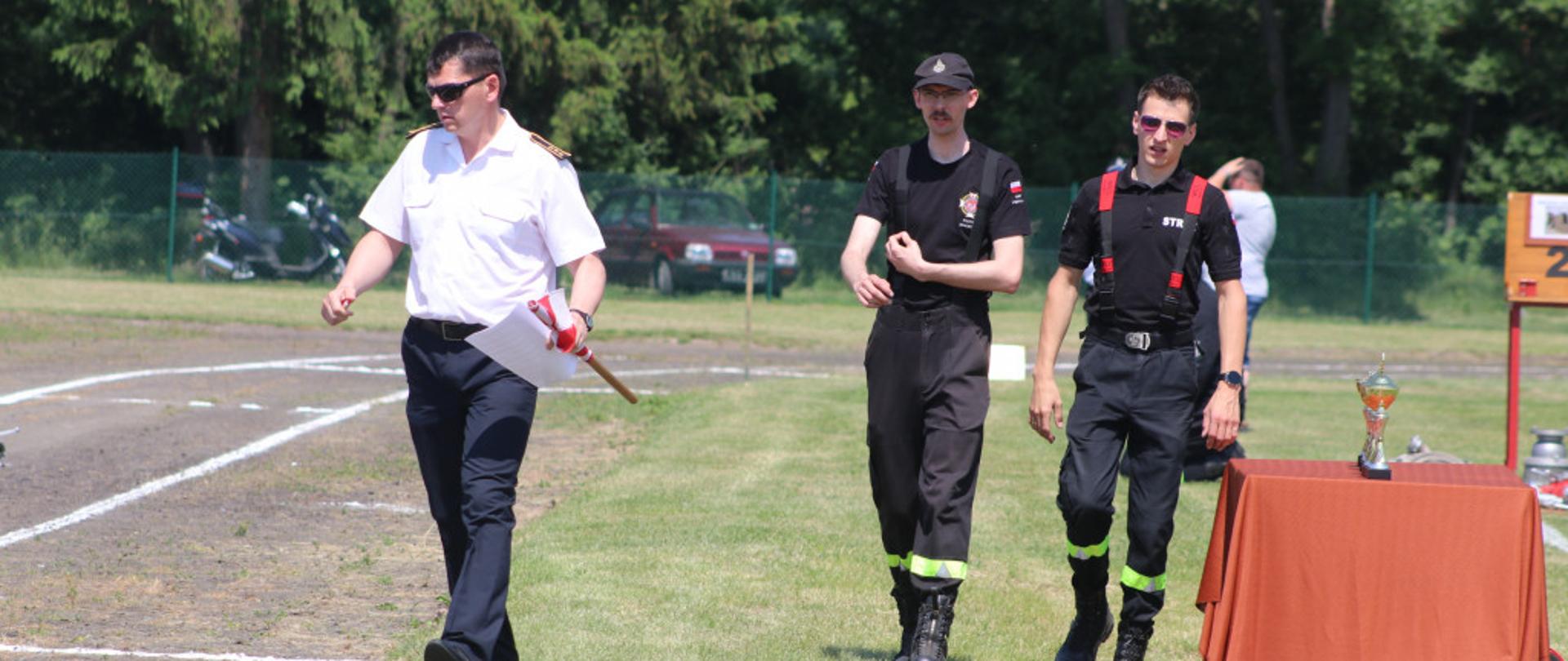 Na zdjęciu znajduje się sędzia zawodów sportowo-pożarniczych oraz dwóch strażaków OSP.