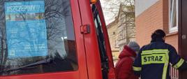  Na zdjęciu widać samochód strażacki oraz osoby biorące udział w akcji dowożenia osób do punktów szczepień. 