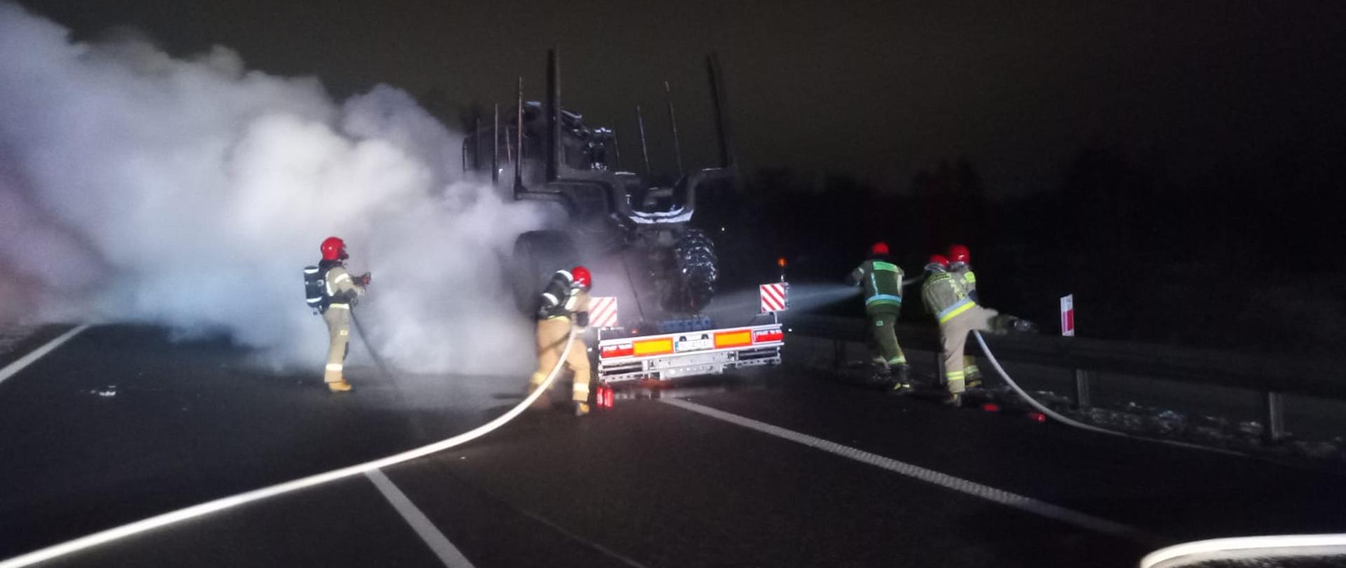 Strażacy gaszą płonącą lawetę, widoczne duże kłęby dymu
