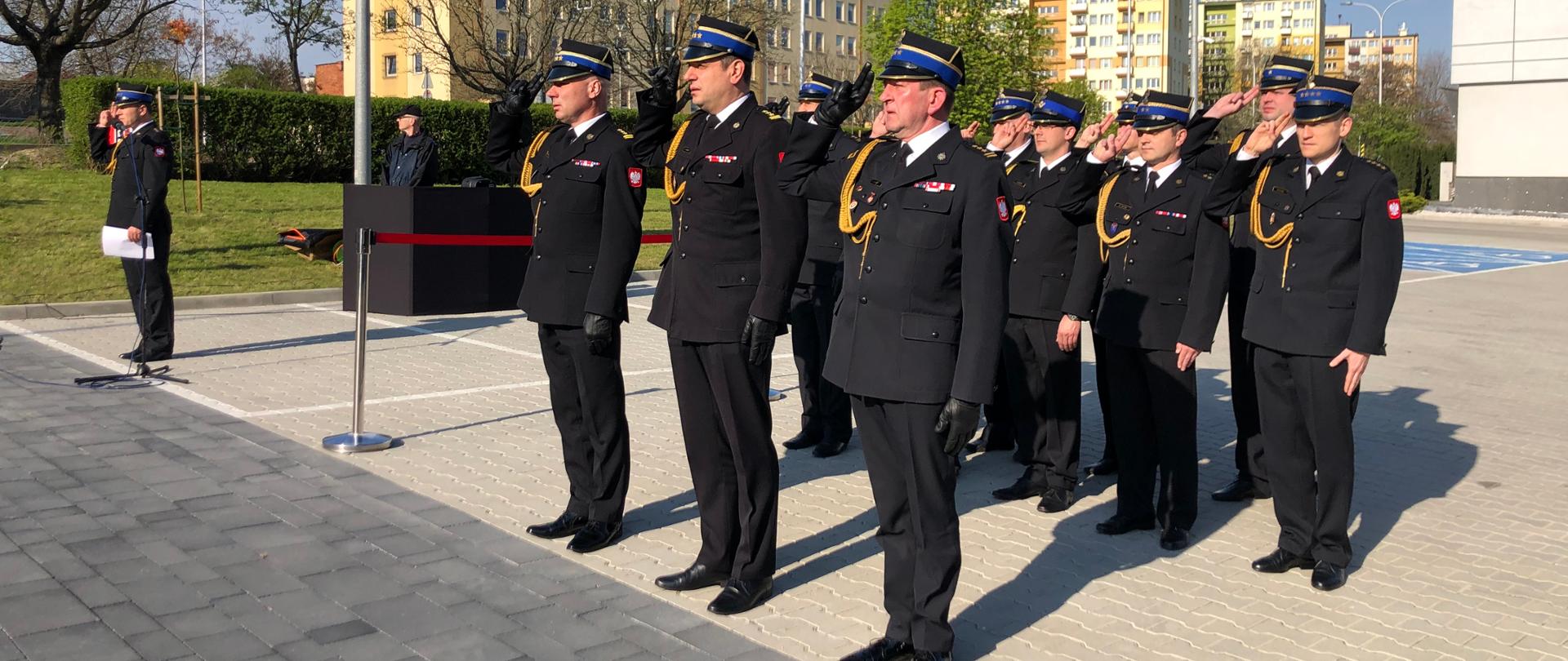 Na zdjęciu widzimy grupę mężczyzn salutujących w mundurach wyjściowych.