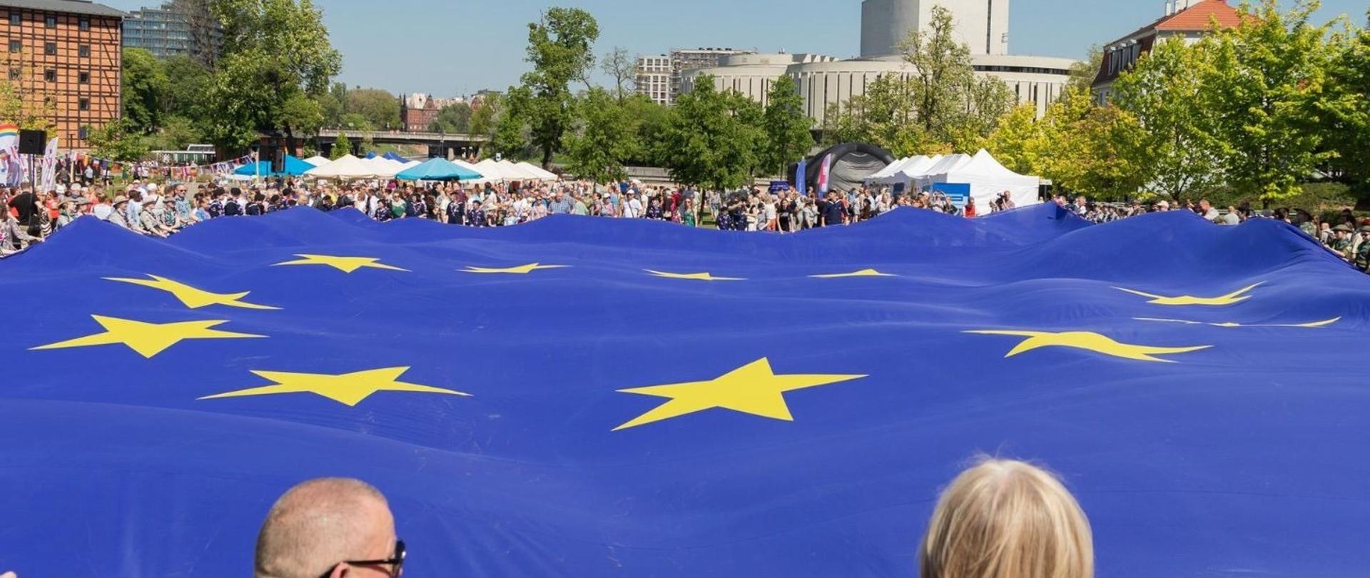 Mieszkańcy Bydgoszczy trzymają wielką flagę Unii Europejskiej na Wyspie Młyńskiej. W tle widać Operę Nova.