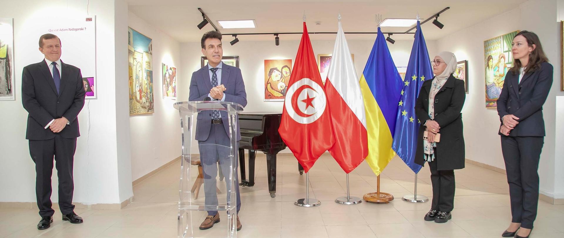 Ambasador UE przemawia za pulpitem, po prawej chargé d’affaires a.i. ambasady RP oraz dyrektorka Maison des Arts du Belvédère, po lewej ambasador Ukrainy. W tle flagi Tunezji, Polski, Ukrainy i Unii Europejskiej oraz obrazy Adama Nidzgorskiego, Marii Prymachenko, Hayet Meddeb Guesmi, Ezzedina Brariego oraz Sema Tareka Chaabane’a.