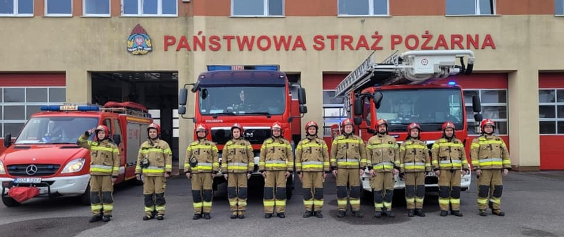 Zdjęcie przedstawia strażaków przed pojazdami ratowniczymi, w trakcie oddawania hołdu strażakom poległym na wojnie w Ukrainie.