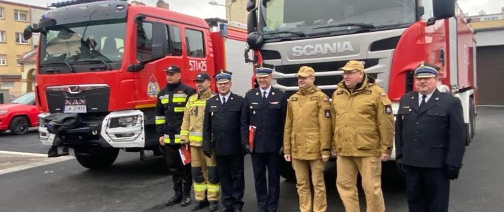 Strażacy - komendanci powiatowi i wojewódzcy na tle przekazywanych pojazdów