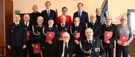 Zdjęcie grupowe uhonorowanych druhen i druhów wraz z osobami wręczającymi na tle sztandaru OSP