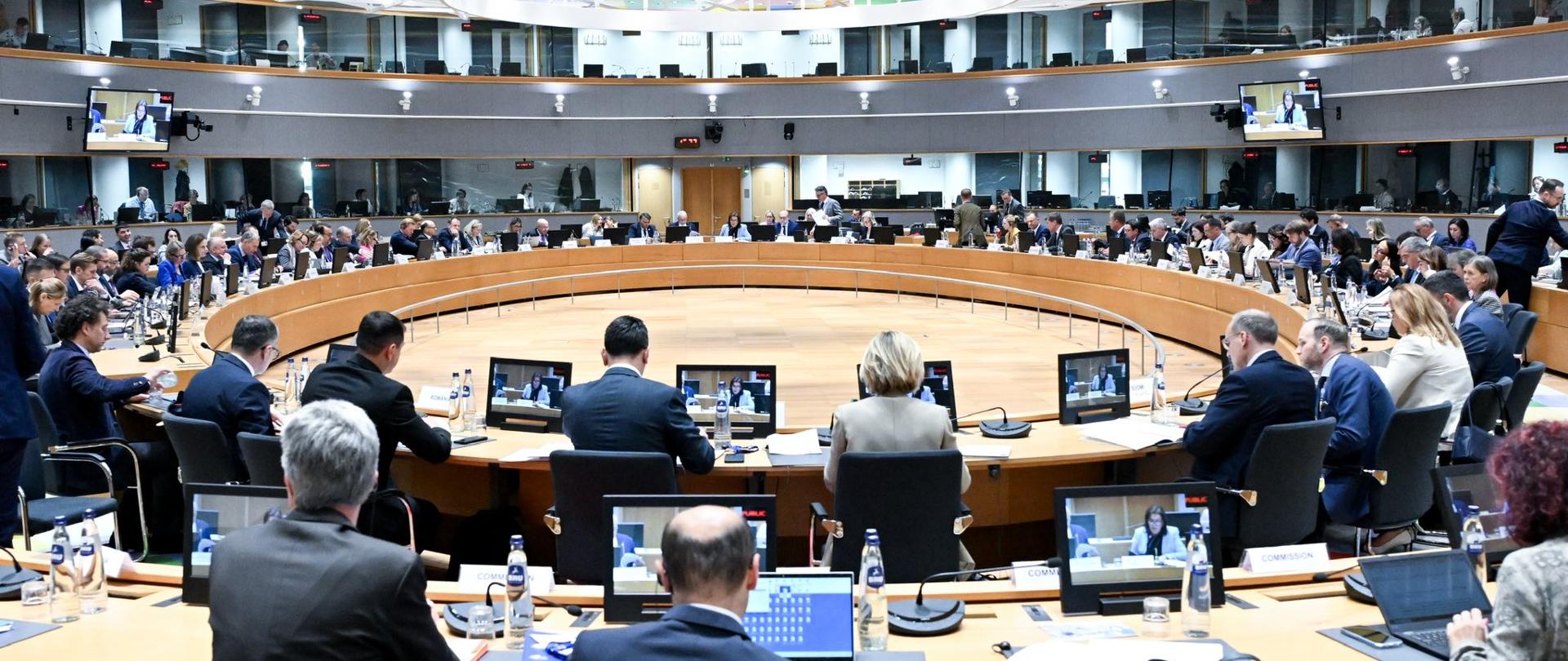 Posiedzenie Rady UE w formacie ministrów ds. sportu. Sala plenarna w Brukseli. Na sali siedzą ludzie w garniturach, przed ekranami komputerów. Okrągła sala z kolorowym sufitem