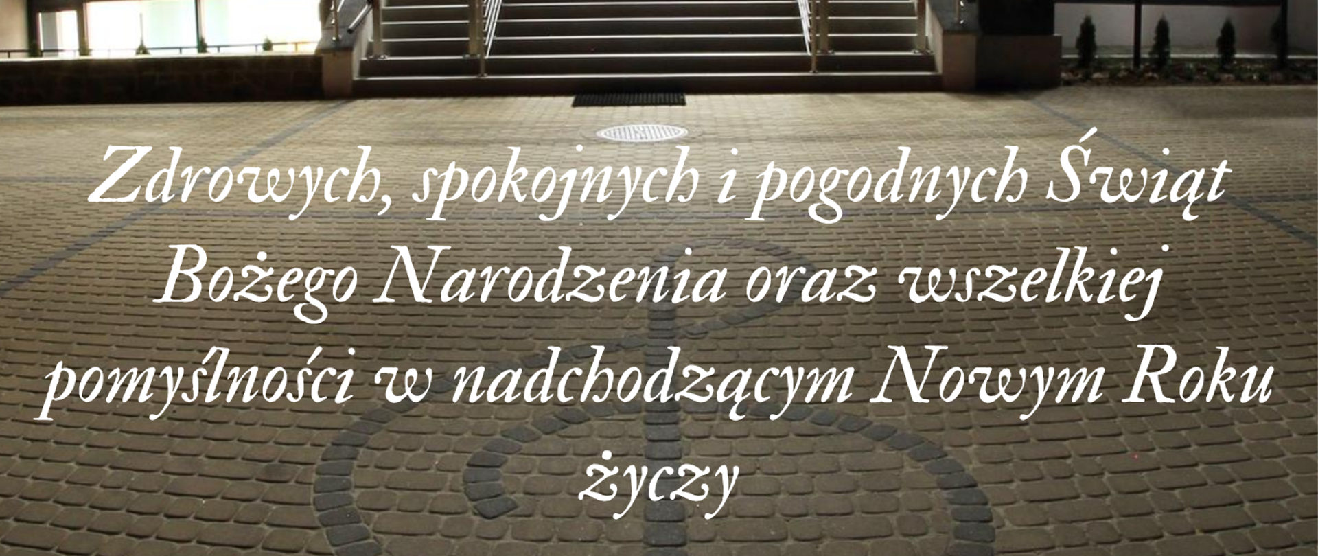 Życzenia z okazji Świąt Bożego Narodzenia na tle zdjęcia oświetlonej szkoły o zmroku