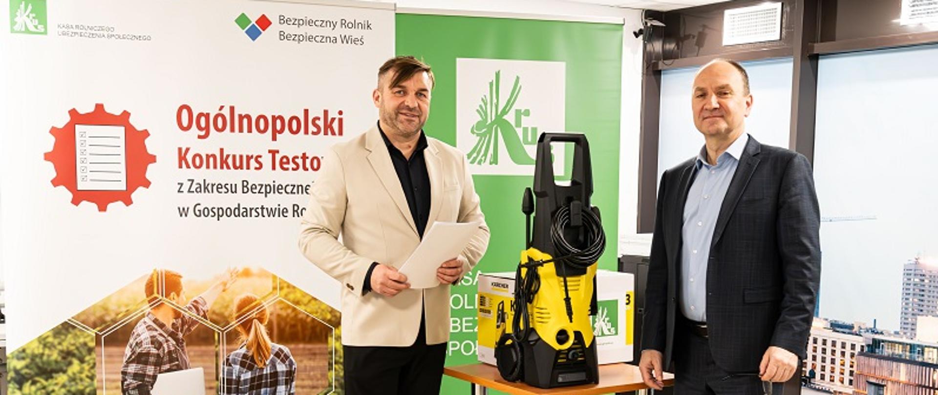 Od lewej: Dyrektor Biura Prewencji KRUS Cezary Nobis oraz Zastępca Prezesa Kasy Rolniczego Ubezpieczenia Społecznego Jacek Paziewski stoją obok stolika z nagrodą w konkursie testowym w postaci myjki ciśnieniowej
