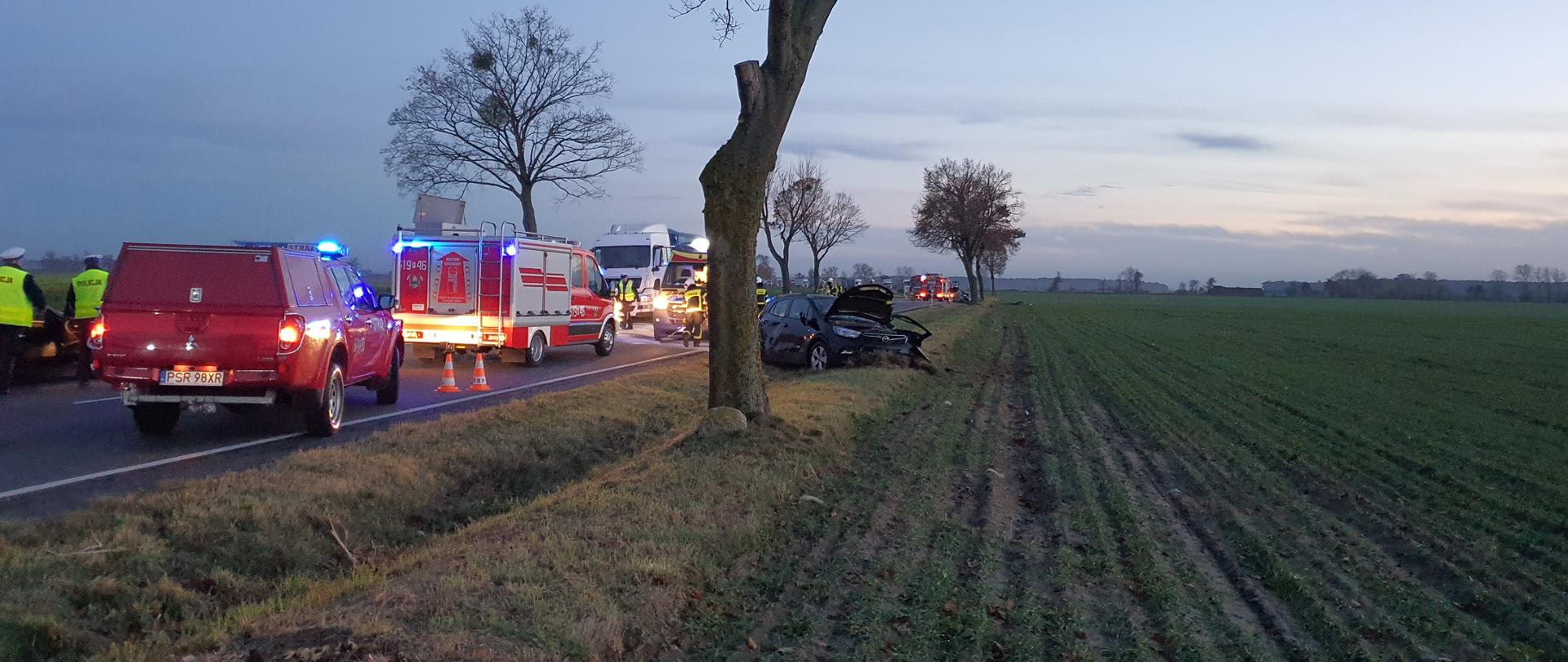 Na zdjęciu pojazdy pożarnicze, karetka pogotowia i strażacy na jezdni podczas akcji ratowniczej