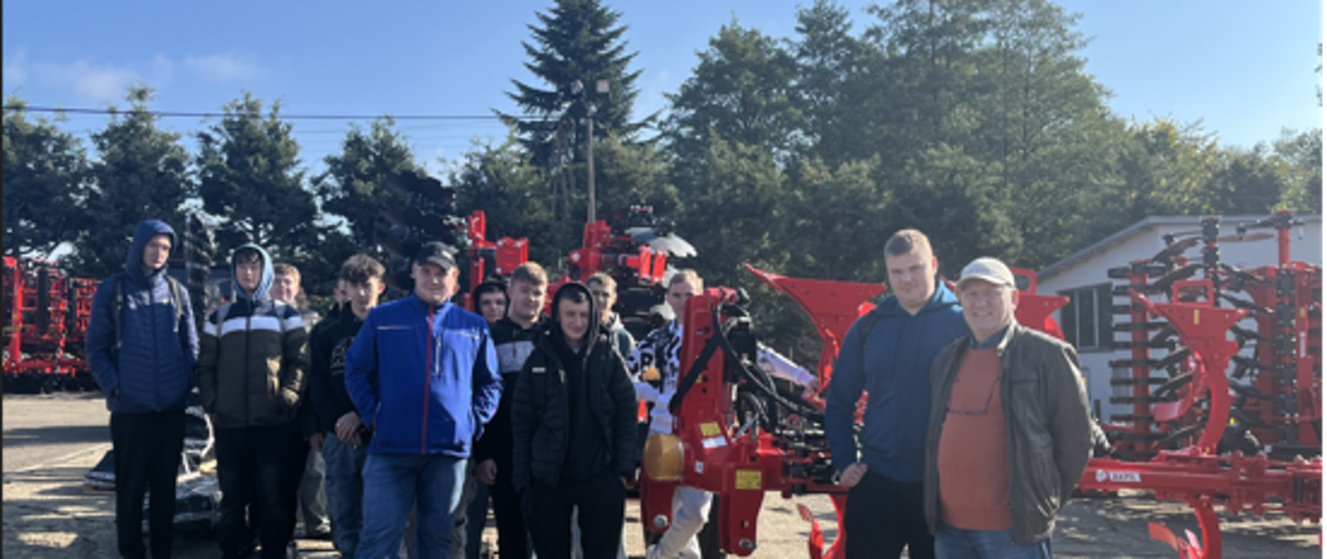 Uczniowie wraz z opiekunem i pracownikami firmy AKPIL na tle ekspozycji maszyn rolniczych