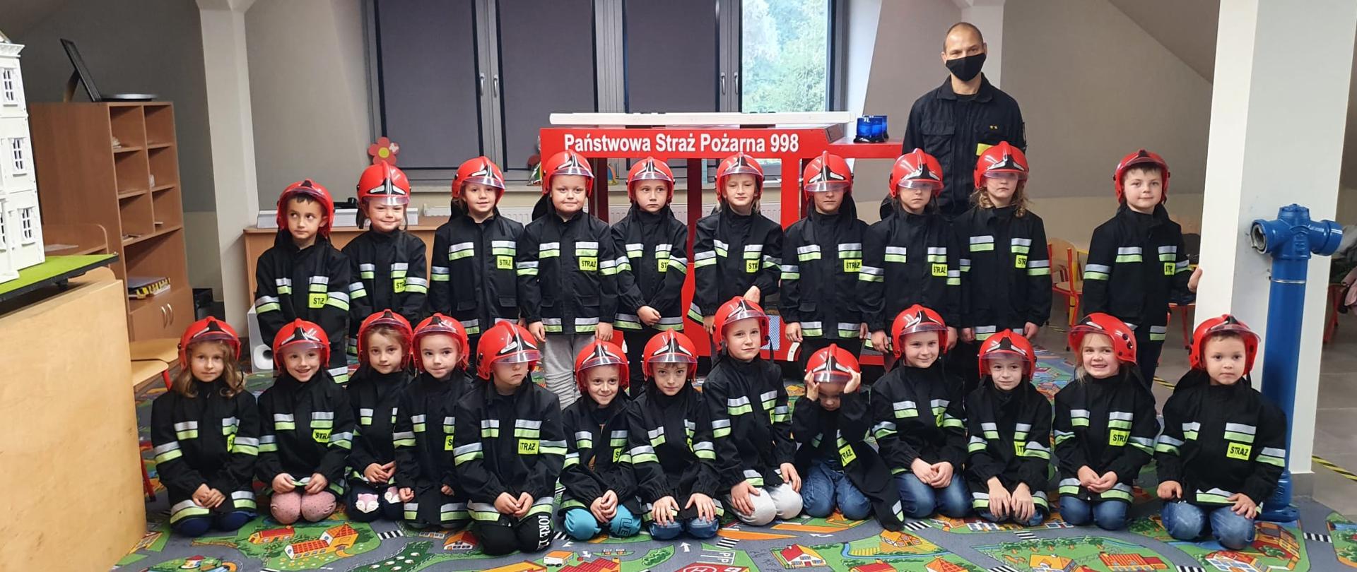 Dzieci ubrane w strój strażaka pozują do zdjęcia ze strażakiem