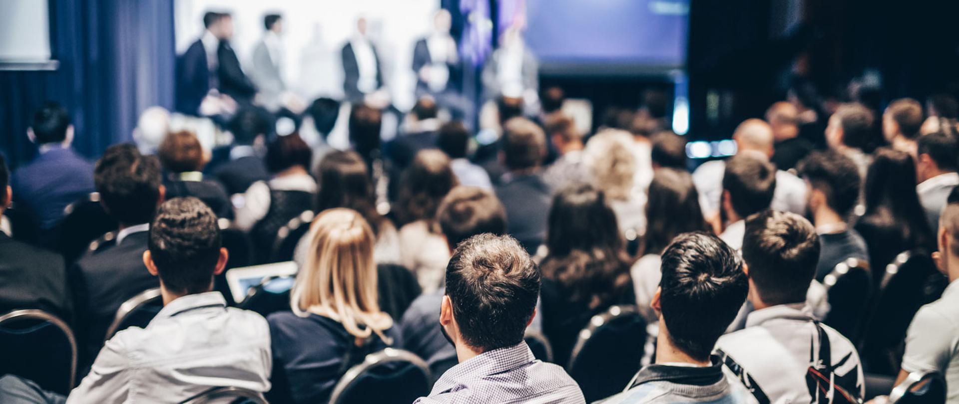 Sala wypełniona ludźmi. Uczestnicy przysłuchują się debacie. 
