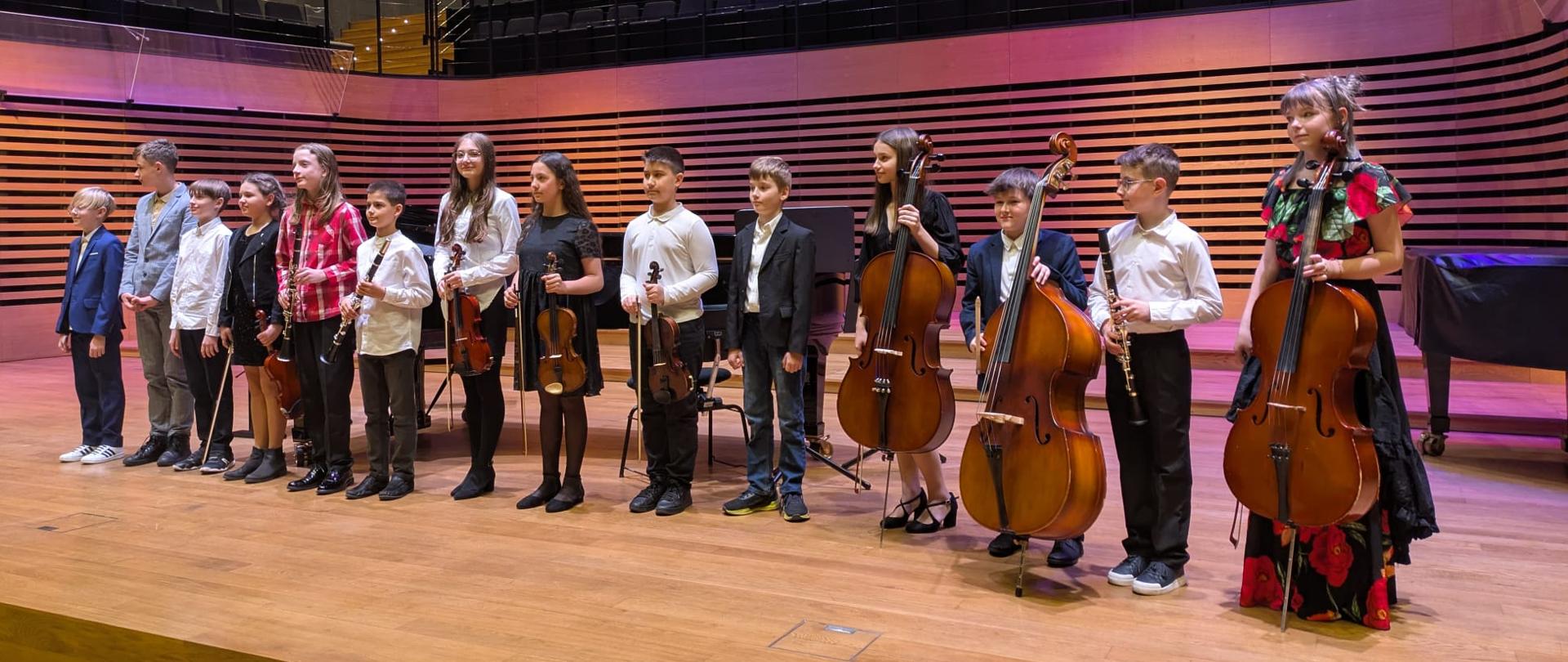 Dzieci stoją w rzędzie na scenie ze swoimi instrumentami.
