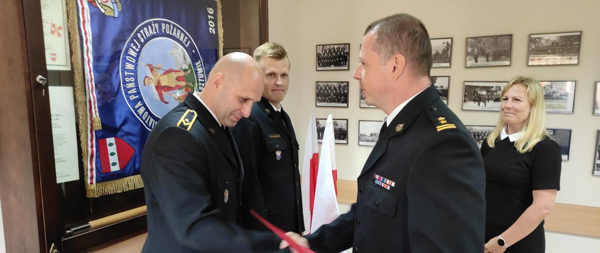 3 osoby w sali wręczają awanse