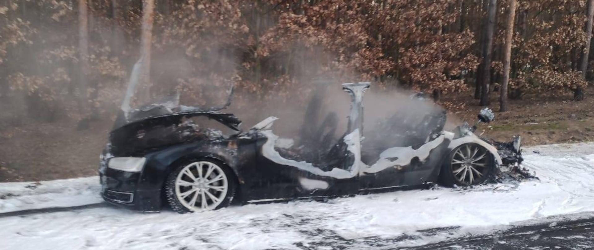 Spalony samochód osobowy, widok z boku, w tle las