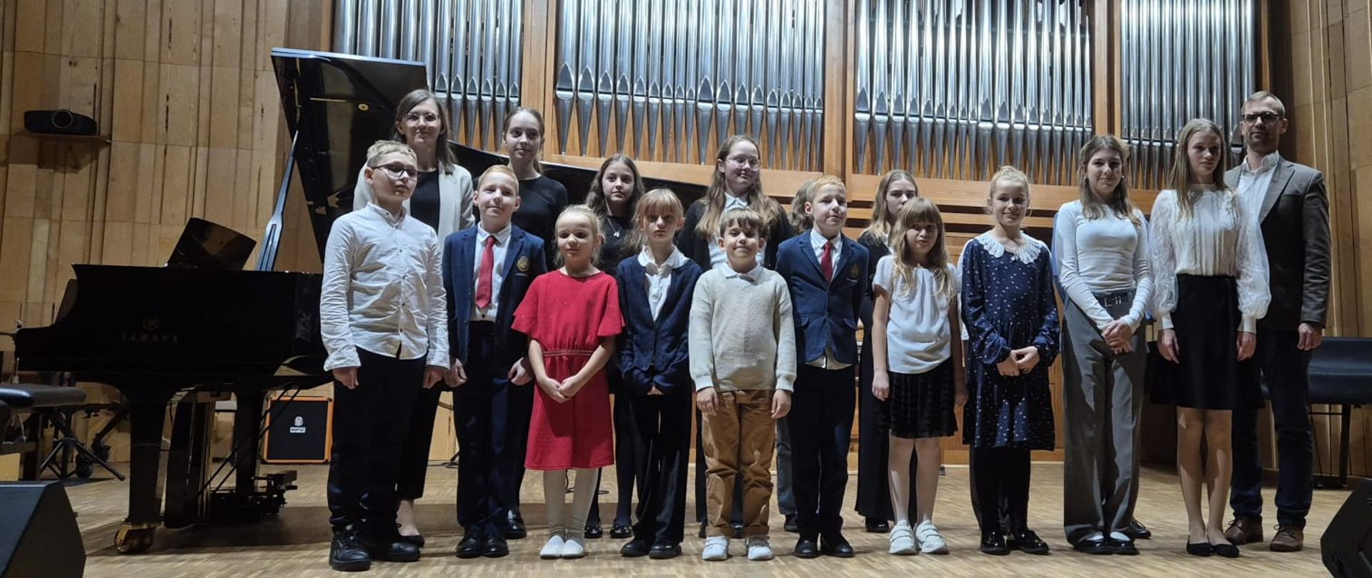 Grupa uczniów na scenie sali koncertowej, w tle organy