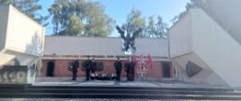 Żołnierze w mundurach stoją na warcie przed pomnikiem.