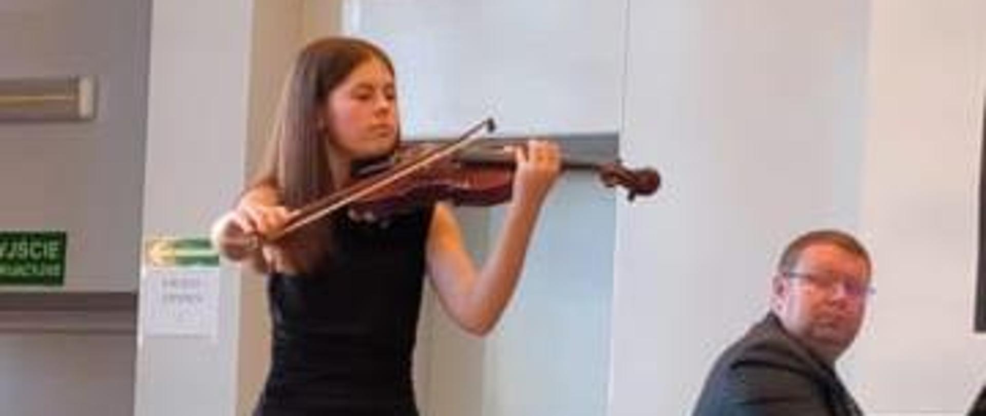 Dziewczyna gra na skrzypcach, mężczyzna akompaniuje na fortepianie.