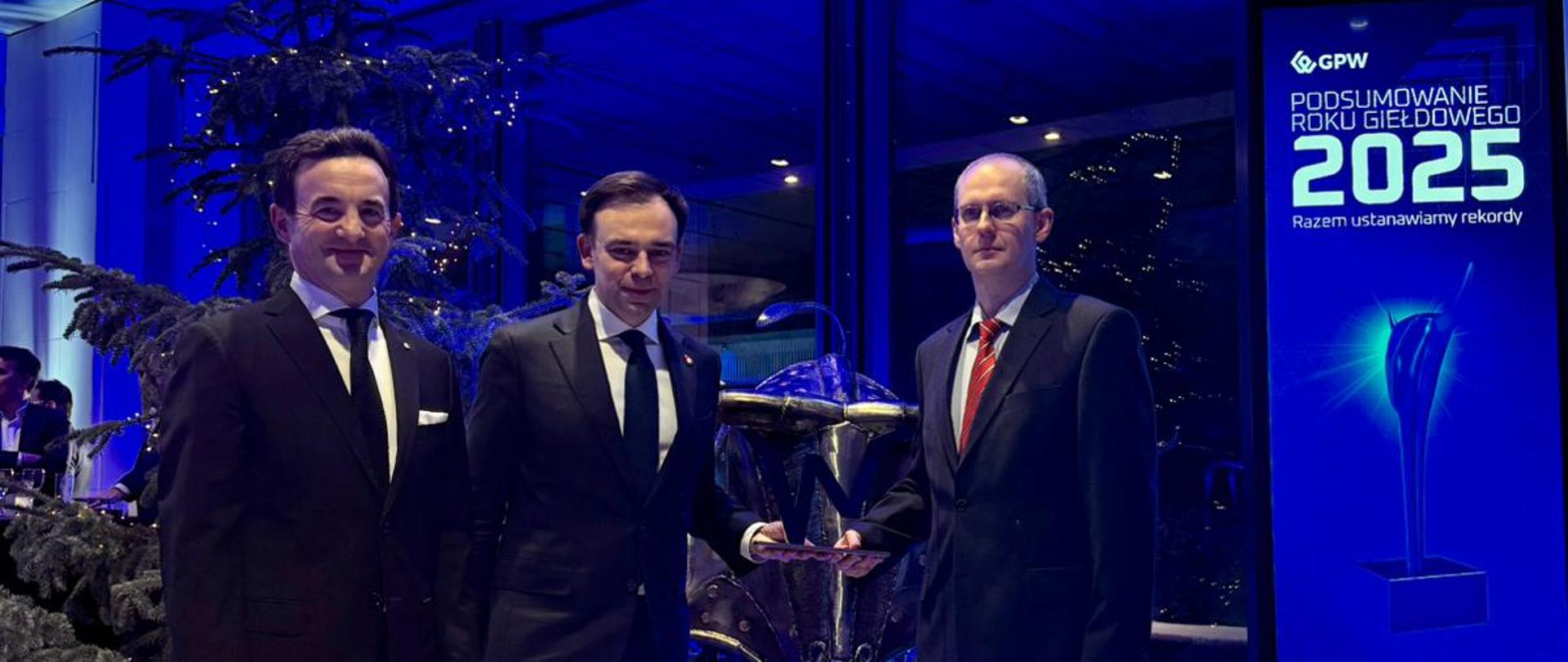 Minister Andrzej Domański podczas Gali Podsumowania Roku Giełdowego 2025, w sali, w tle choinki, obok baner z nazwą gali