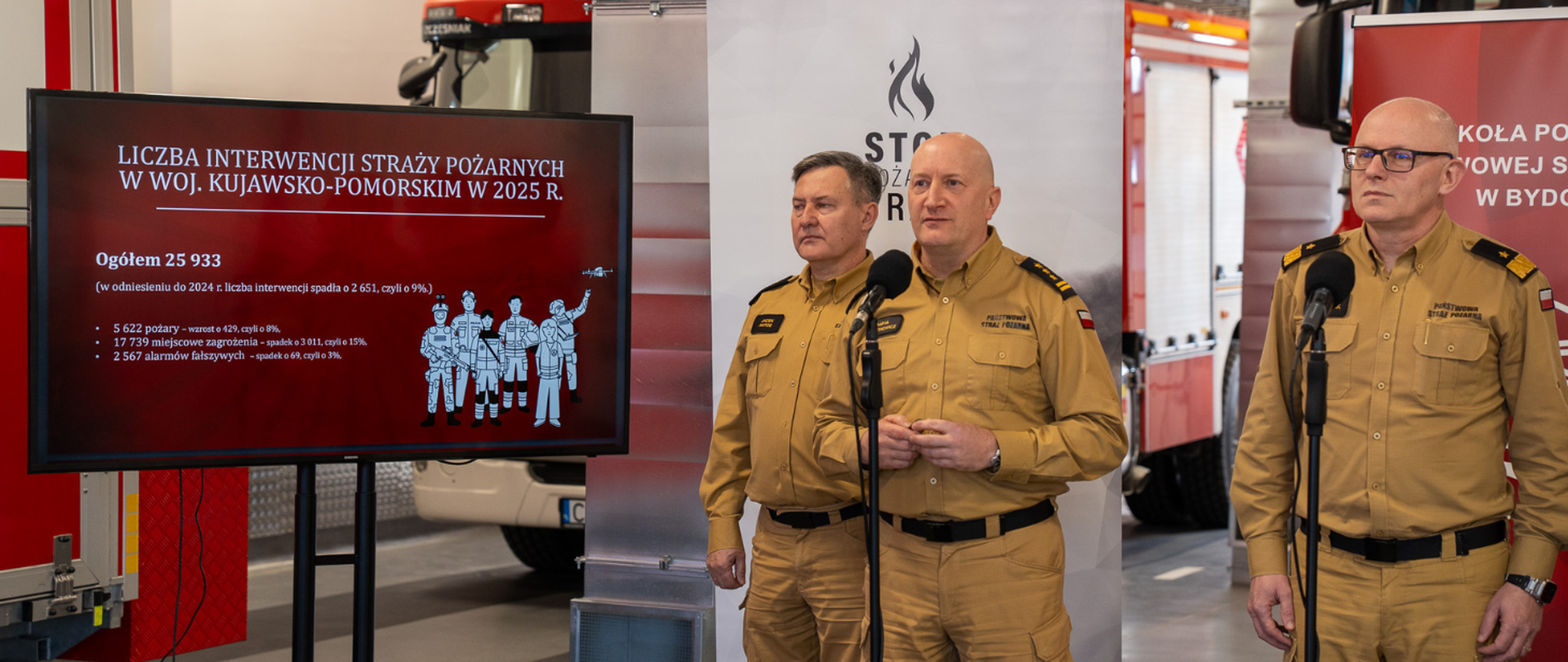 Konferencja prasowa Państwowej Straży Pożarnej. Od lewej stoją osoby pracujące w PSP, stoją w mundurach wyjściowych: Kujawsko-Pomorski Komendant Wojewódzki st. bryg. Rafał Świechowicz, Zastępca Komendanta Głównego PSP nadbryg. Paweł Frysztak oraz Komendant Szkoły Podoficerskiej PSP w Bydgoszczy st. bryg. Jacek Antos. Po prawej stronie stoi Wicewojewoda Kujawsko-Pomorski Michał Koniuch w ciemnym garniturze. W tle widoczne są oficjalne rollupy z logo i napisem Państwowa Straż Pożarna.