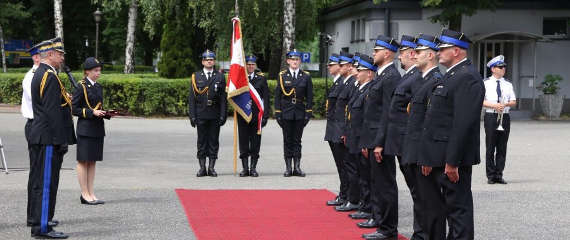 po prawo absolwenci CSPSP ustawieni w szeregu do promocji, na wprost poczet sztandarowy, po lewo zastępca komendanta głównego przemawia do mikrofonu, obok niego stoi funkcjonariusz i funkcjonariuszka