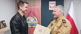 Komendant Powiatowy Państwowej Straży Pożarnej w Człuchowie st. bryg. Radosław Batruch stoi w gabinecie i wręcza akt mianowania mł. ogn. Igorowi Gałan na stanowisko starszy ratownik – kierowca. 