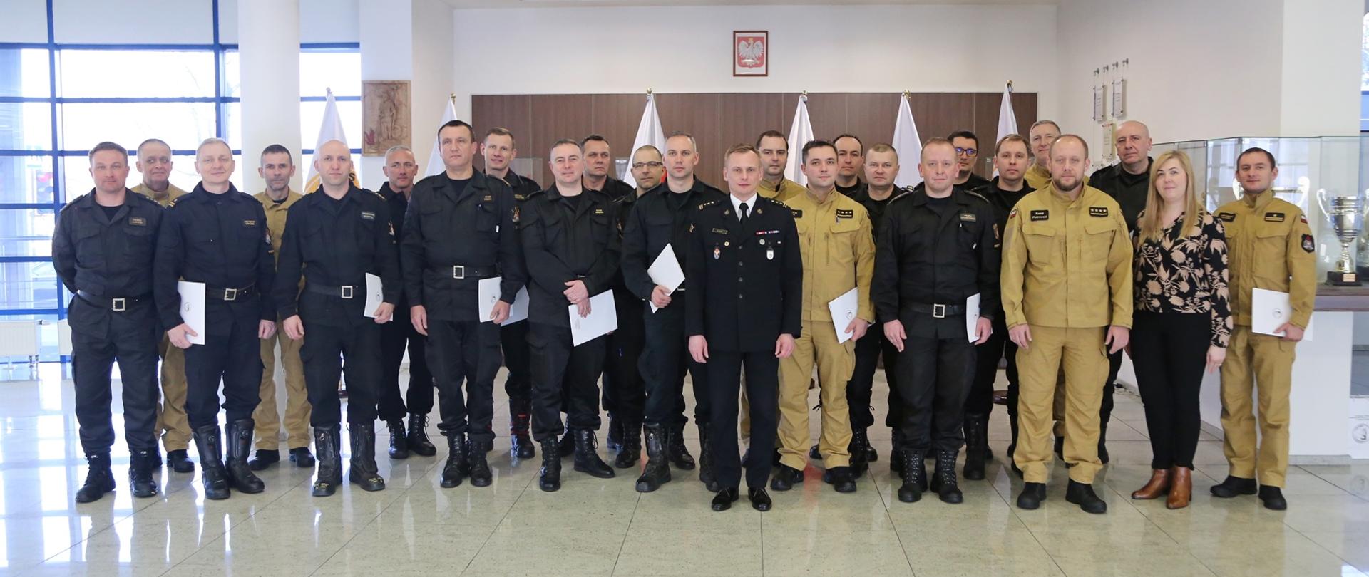 Grupowe zdjęcie uczestników szkolenia (20 funkcjonariuszy PSP) w towarzystwie Zastępcy Komendanta Centralnej Szkoły PSP, trzech oficerów CS PSP oraz kobiety