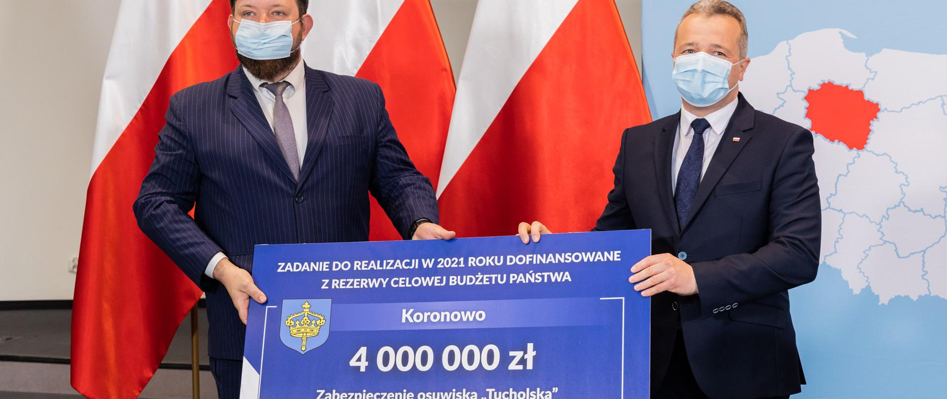 Wojewoda kujawsko-pomorski i burmistrz gminy Koronowo trzymają planszę informująco o kwocie wsparcia Gminy Koronowo 