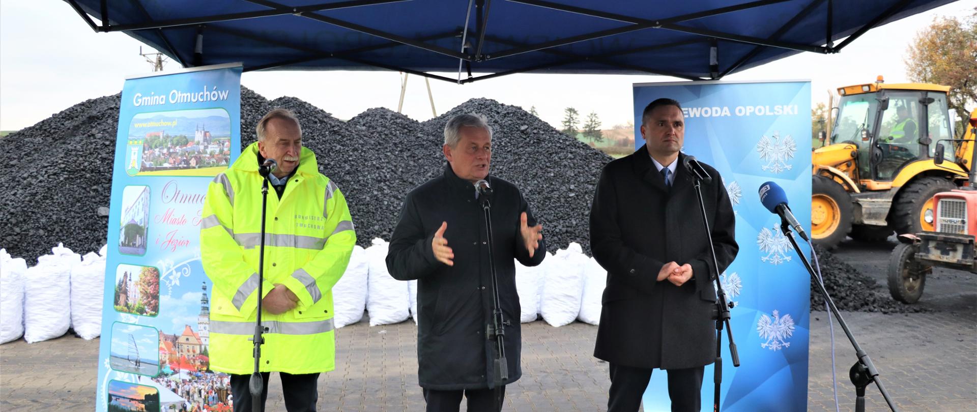 Trzech mężczyzn stojących przed hałdą węgla