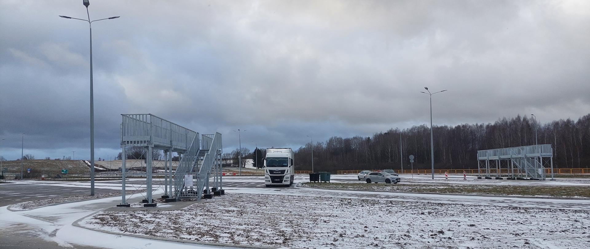 Stalowy pomost ze schodkami, zabezpieczony barierkami, ustawiony na wysokości dachu ciężarówki i górnej części naczepy tak, aby można było ją ręcznie odśnieżyć. W tle ciężarówka. 