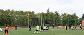 Zawodnicy w strojach czarno-białych oraz zielono-białych grają w piłkę nożna na boisku.