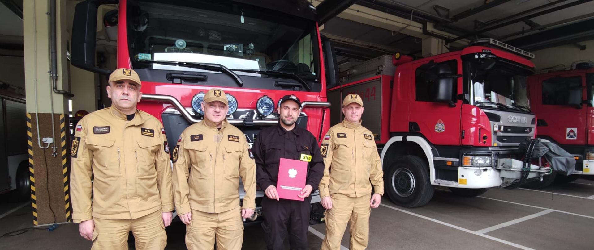 Komendant miejski PSP, zastępca komendanta, dowódca JRG oraz Adrian Petryczko stoją w garażu JRG 1 
