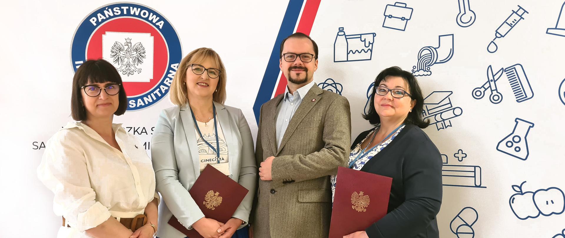 Zdjęcie wyróżnionych kobiet Anny Tymoczko i Anny Tkaczyk trzymających w rękach dyplomy Wojewody Mazowieckiego. Obok stoją dyrektor WSSE w Warszawie dr. n. med. Przemysław Rzodkiewicz oraz Z-ca Dyrektora ds. laboratorium Anna Krawczuk.