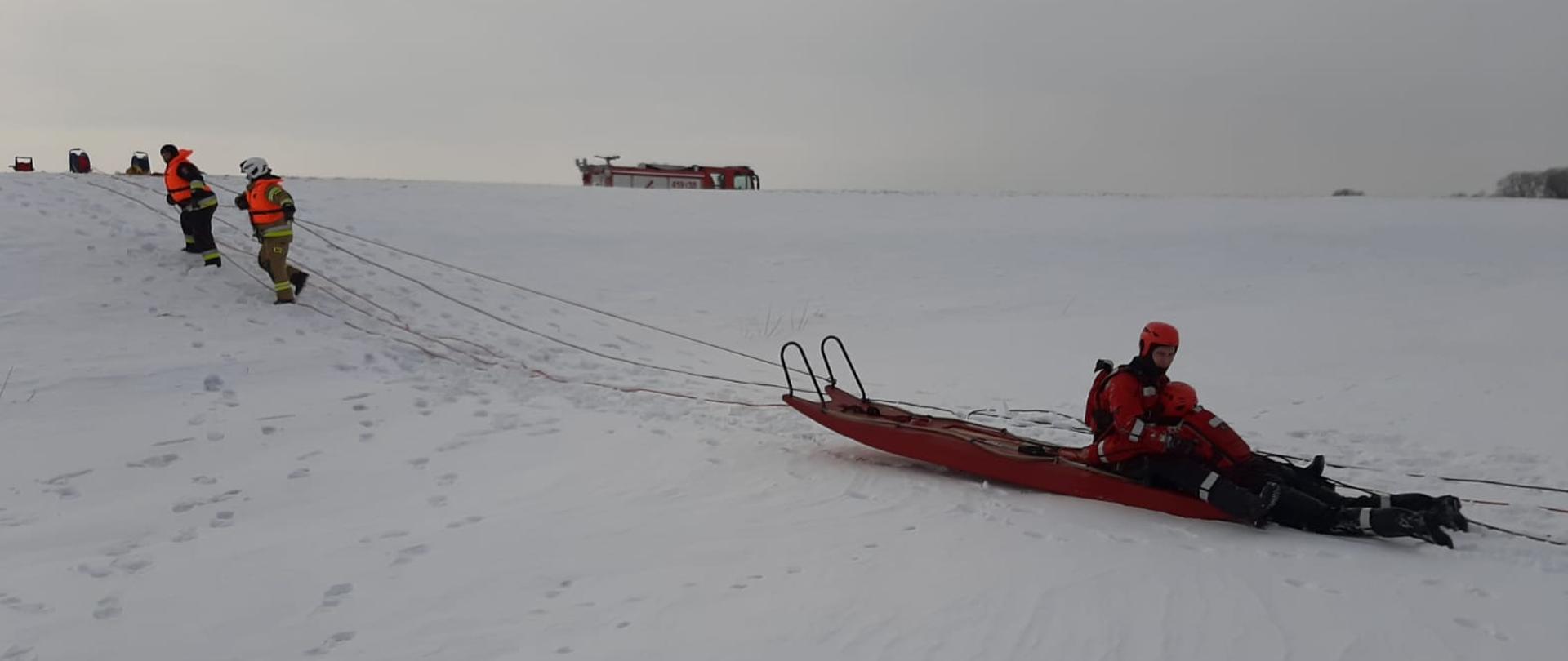 Ewakuacja pozoranta przez 3 strażaków przy użyciu sań lodowych na zamarzniętym akwenie wodnym