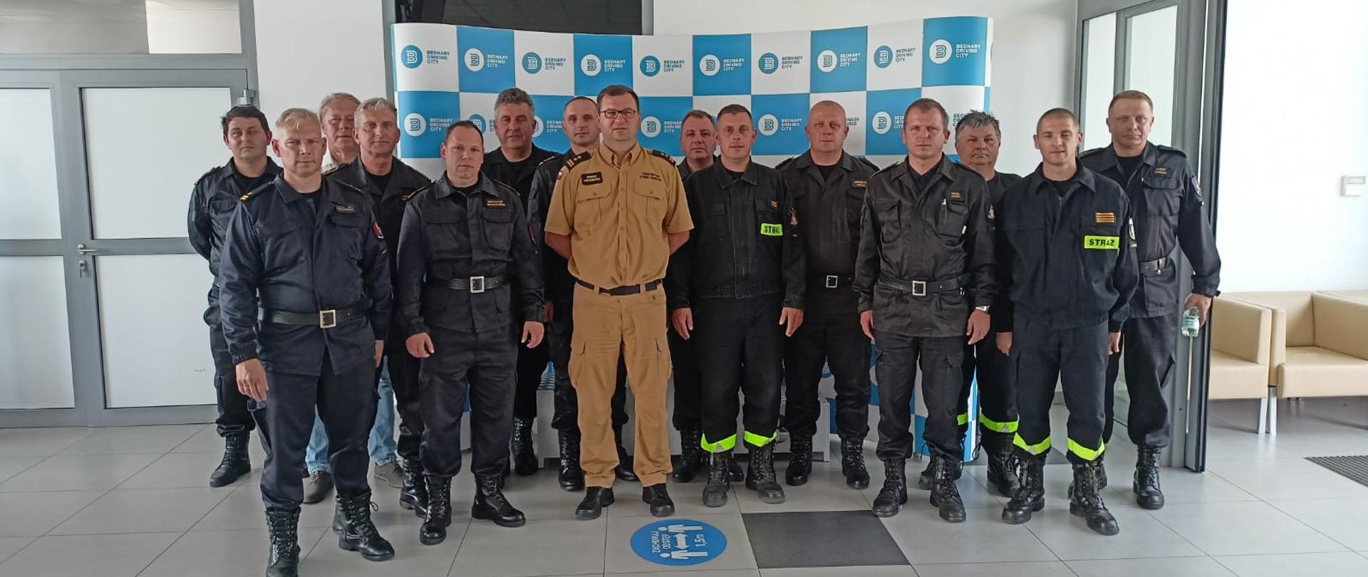 Strażacy w mundurach stoją w dwuszeregu w pomieszczeniu.