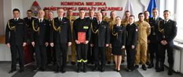 Grupa strażaków i funkcjonariuszy PSP pozuje do wspólnego zdjęcia po ceremonii ślubowania, stojąc w sali komendy w Skierniewicach