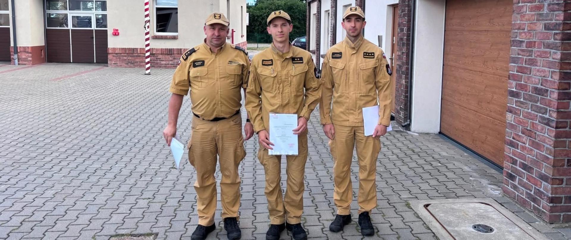 Na zdjęciu Komendant Powiatowy PSP w Pucku bryg. Wojciech Wanat, Dowódca JRG w Pucku st. kpt. Maciej Humanowski oraz mł. kpt. Grzegorz Brzeziński. Wszyscy ubrani w stroje koszarowe w kolorze piaskowym, na drugim planie budynek Komendy Powiatowej PSP w Pucku.