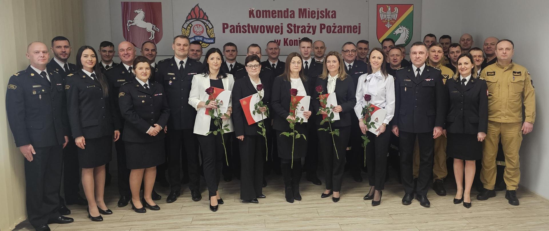 Strażacy oraz pracownicy cywilni stoją w świetlicy podczas uroczystej zbiórki z okazji Dnia Służby Cywilnej