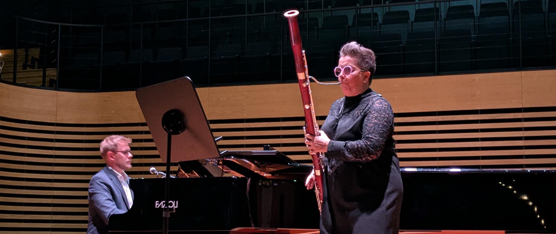 Kobieta gra na fagocie, mężczyzna jej akompaniuje na fortepianie.